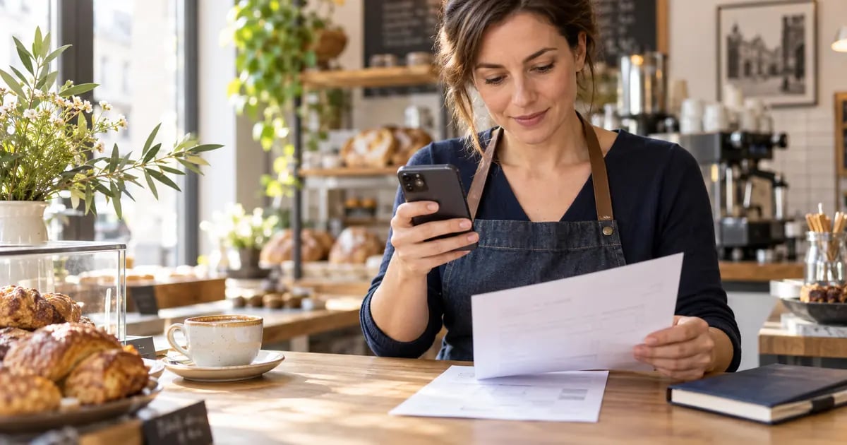 A cafe owner reviews an invoice and a banking screen before making a transfer.
